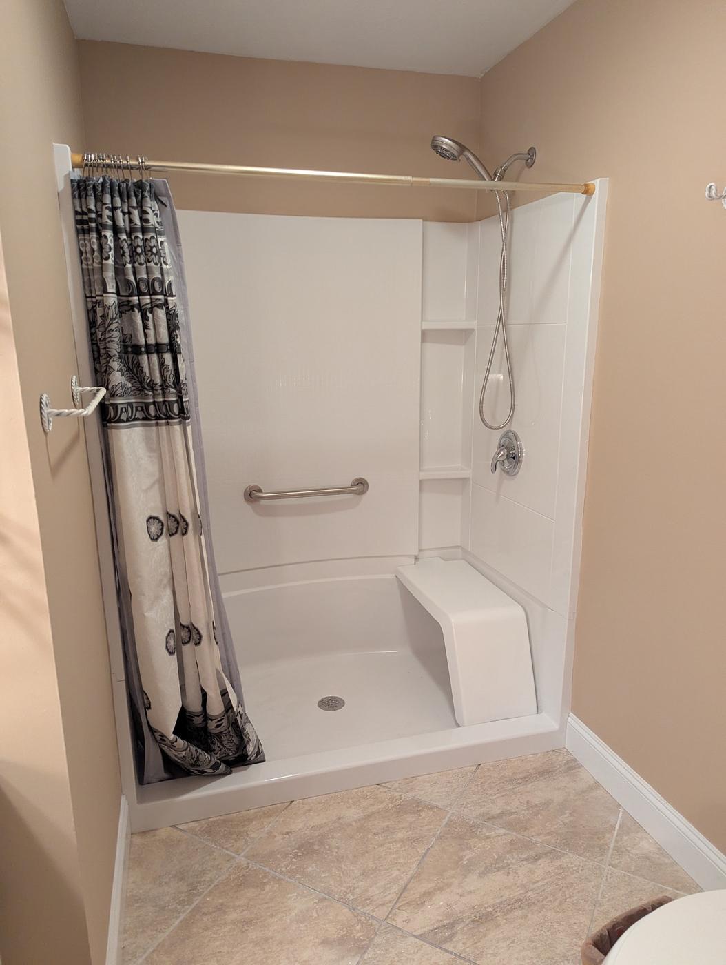 A finished shower with a low step, a built-in seat, a grab bar and a handheld on a slide bar