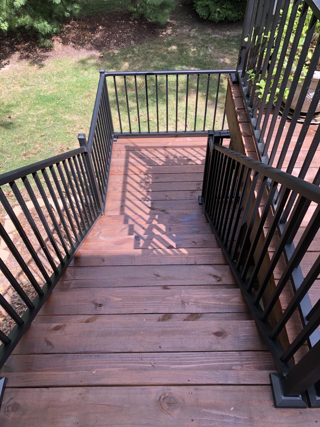 A deck freshly refinished in a deep red-brown, looking down the steps between black metal balusters